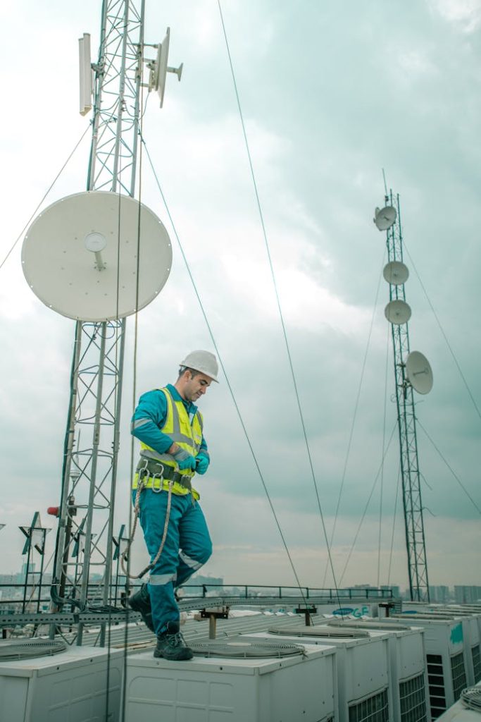 Telecommunications worker in Shaqlawa adjusting equipment on rooftop, wearing safety gear.