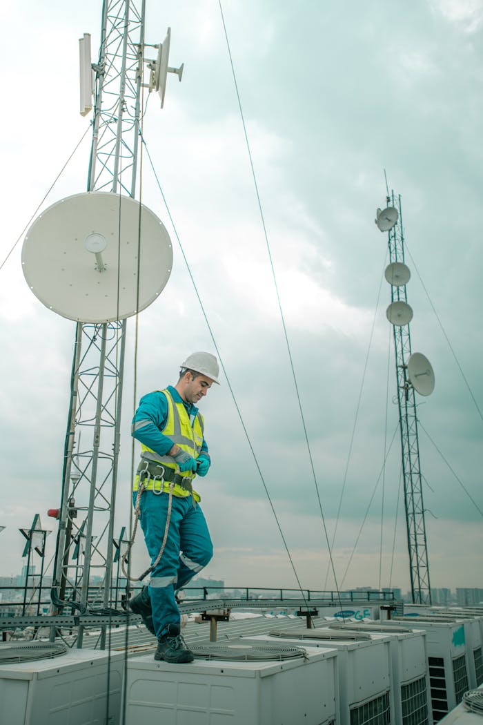 mobile-02 Telecommunications worker in Shaqlawa adjusting equipment on rooftop, wearing safety gear.